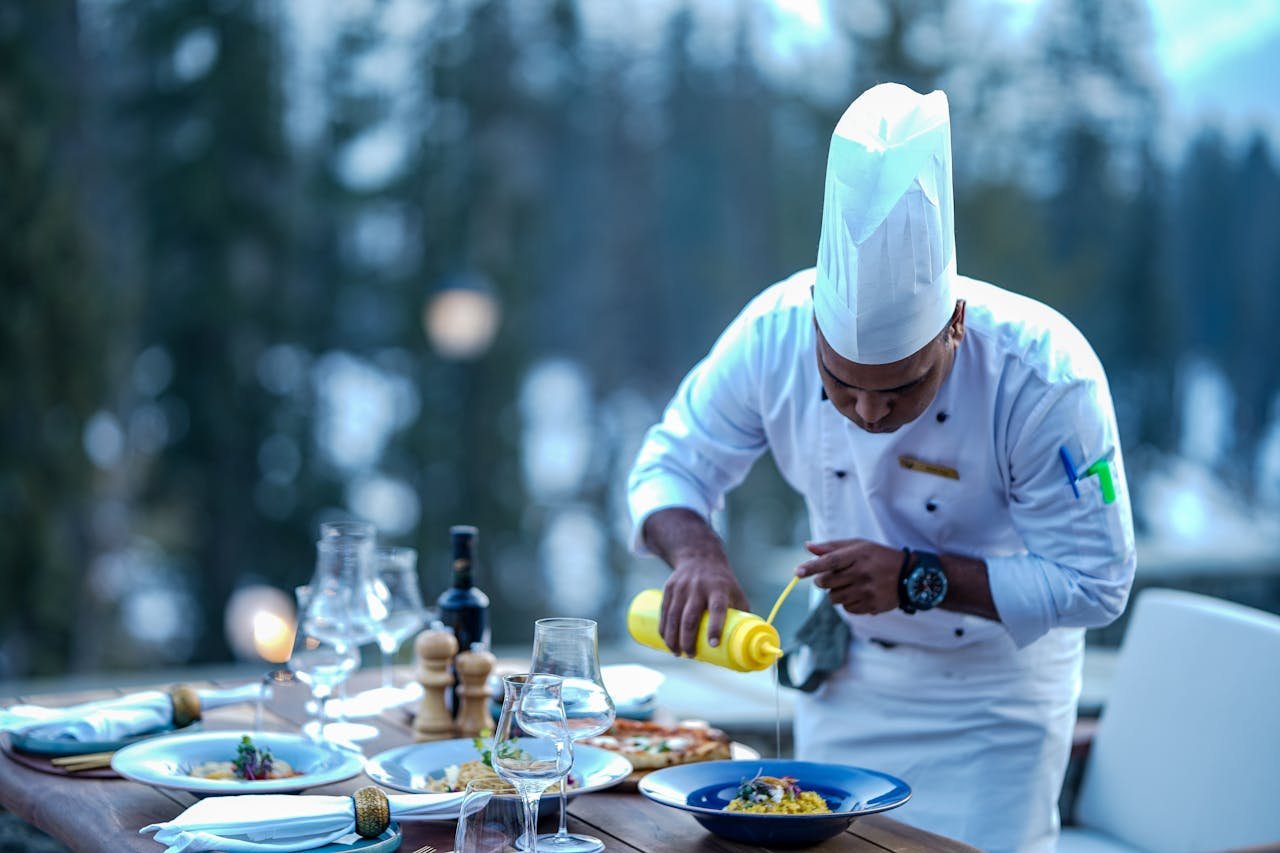 Chef expertly adds finishing touches to a gourmet dish at an outdoor restaurant setting.