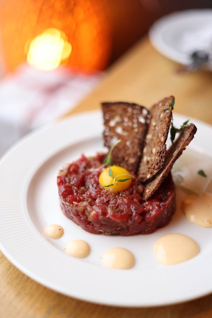 Delicious gourmet beef tartare topped with a quail egg and rye crisps, elegantly plated.