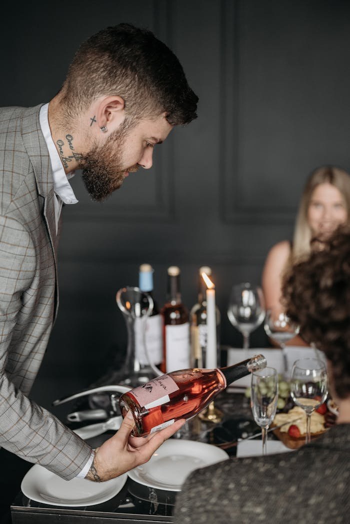 About Caucasian man with tattoos serves wine at an elegant indoor dinner gathering.